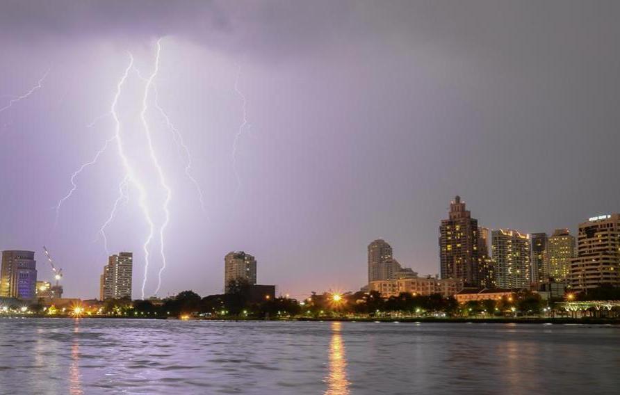 Cityscape with purple overcast sky and lightning striking over water